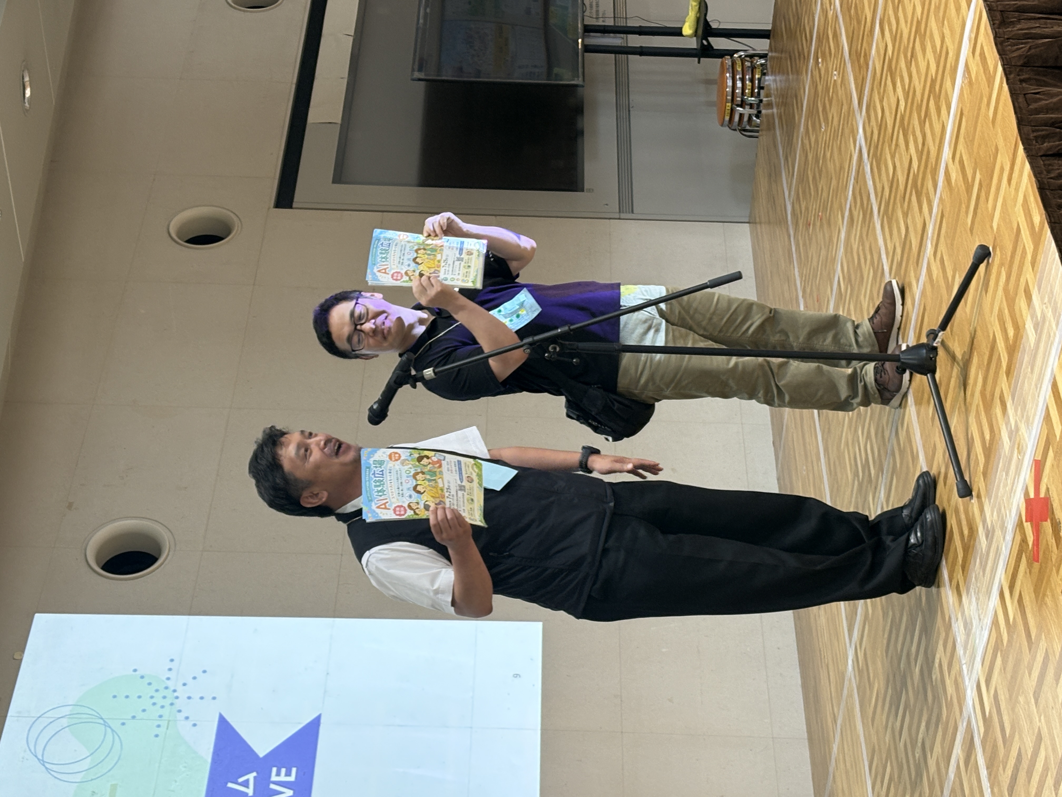 ムーブフェスタ会場のステージで「AI体験広場」のチラシを掲げてPRする様子